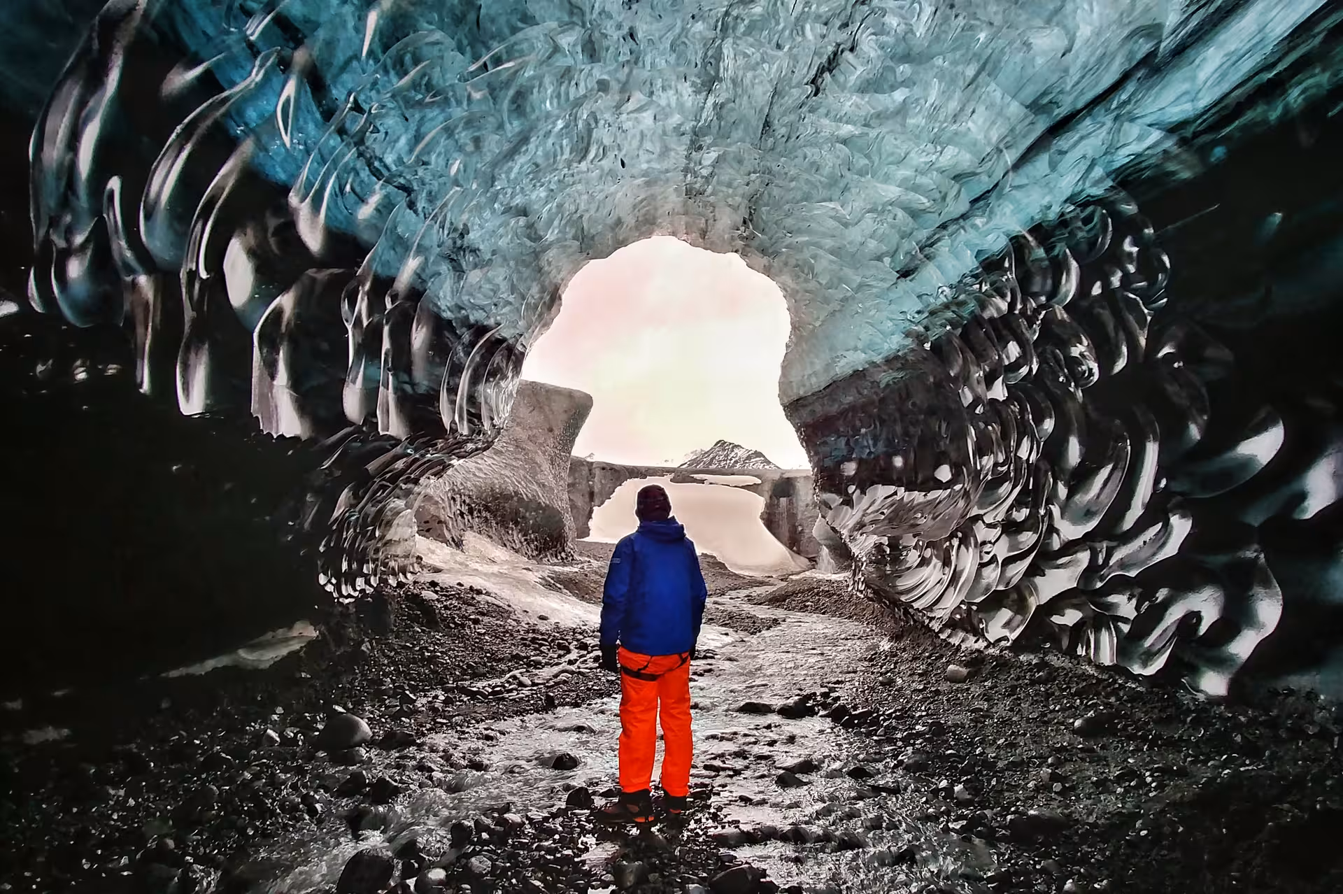 Explorer in blue jacket standing inside Vatnajokull glacier ice cave tunnel with turquoise ice walls