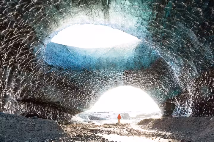 Person standing inside massive Vatnajokull glacier ice cave with textured blue ice walls and bright opening