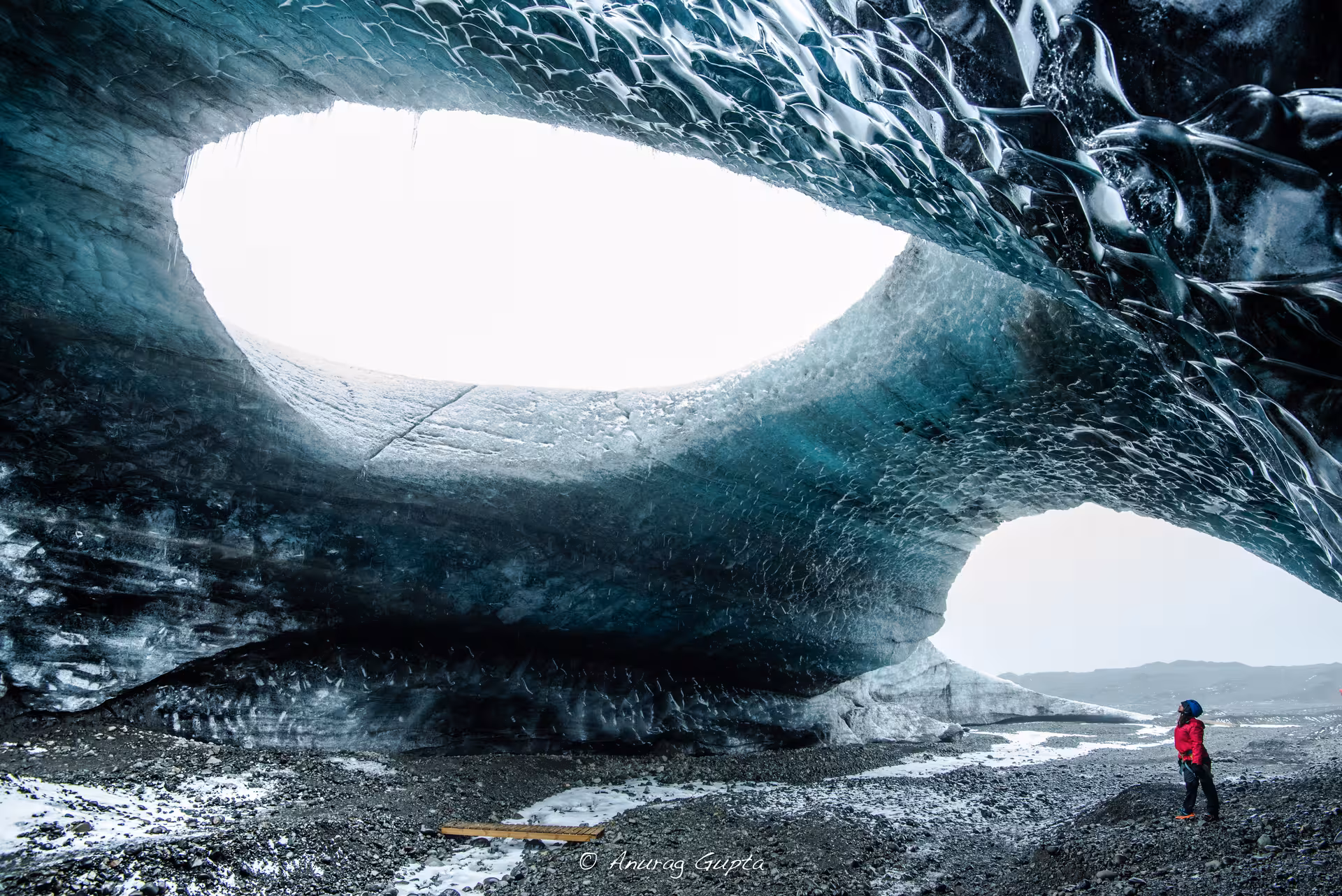 Explorer in red jacket standing inside a massive Vatnajokull glacier ice cave with two openings in Iceland