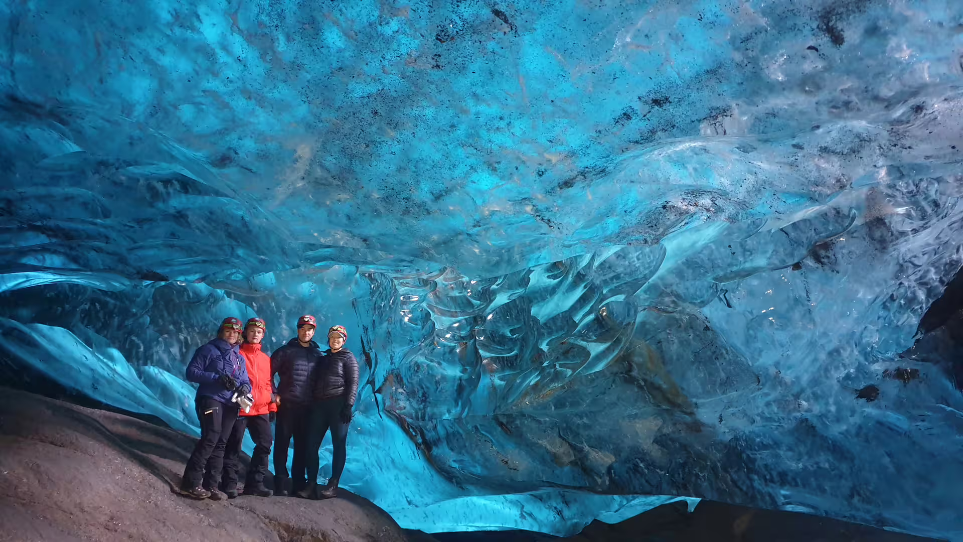Four tourists in helmets posing inside a stunning blue glacial ice cave at Vatnajokull, Iceland