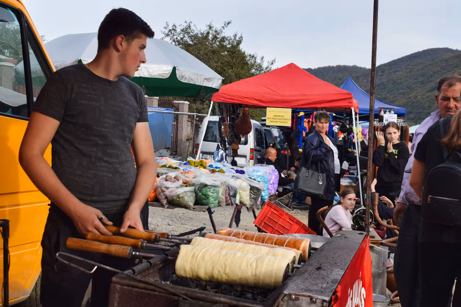Young vendor grilling kürtőskalács chimney cake at colorful Negreni Flea Market guided tour in Romania