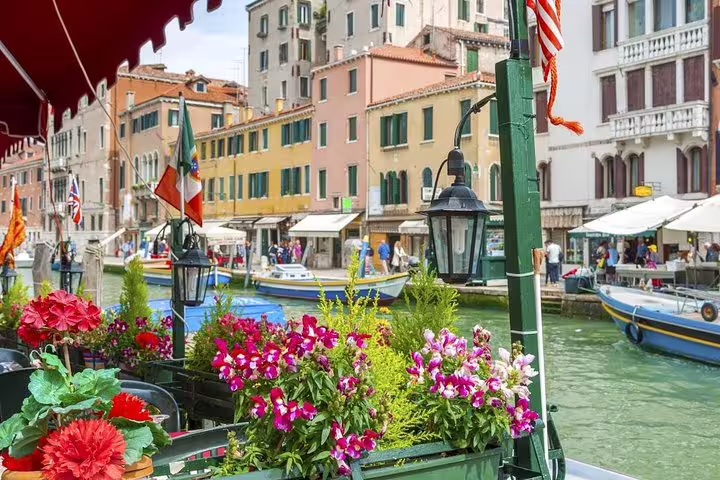 Colorful flowers on a quiet canal-side terrace in Venice with boats and pastel houses on a private off-the-beaten-path tour