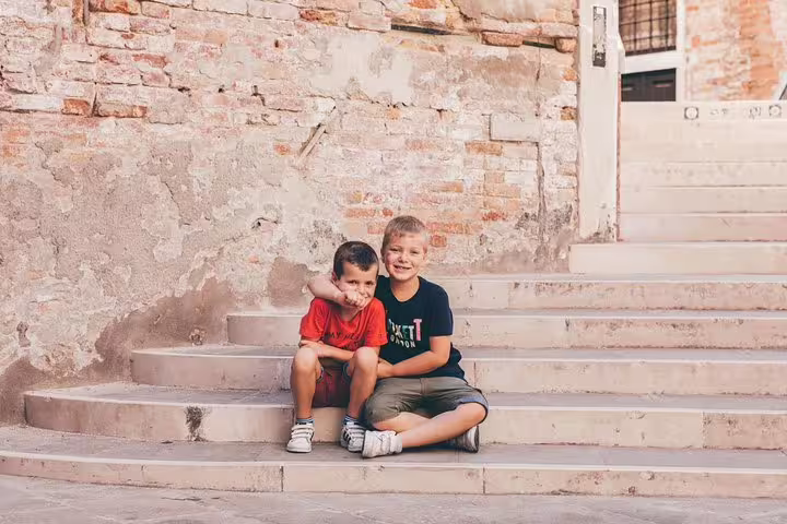 Two boys sitting on Venice steps by rustic brick wall, family photo session with personal travel photographer
