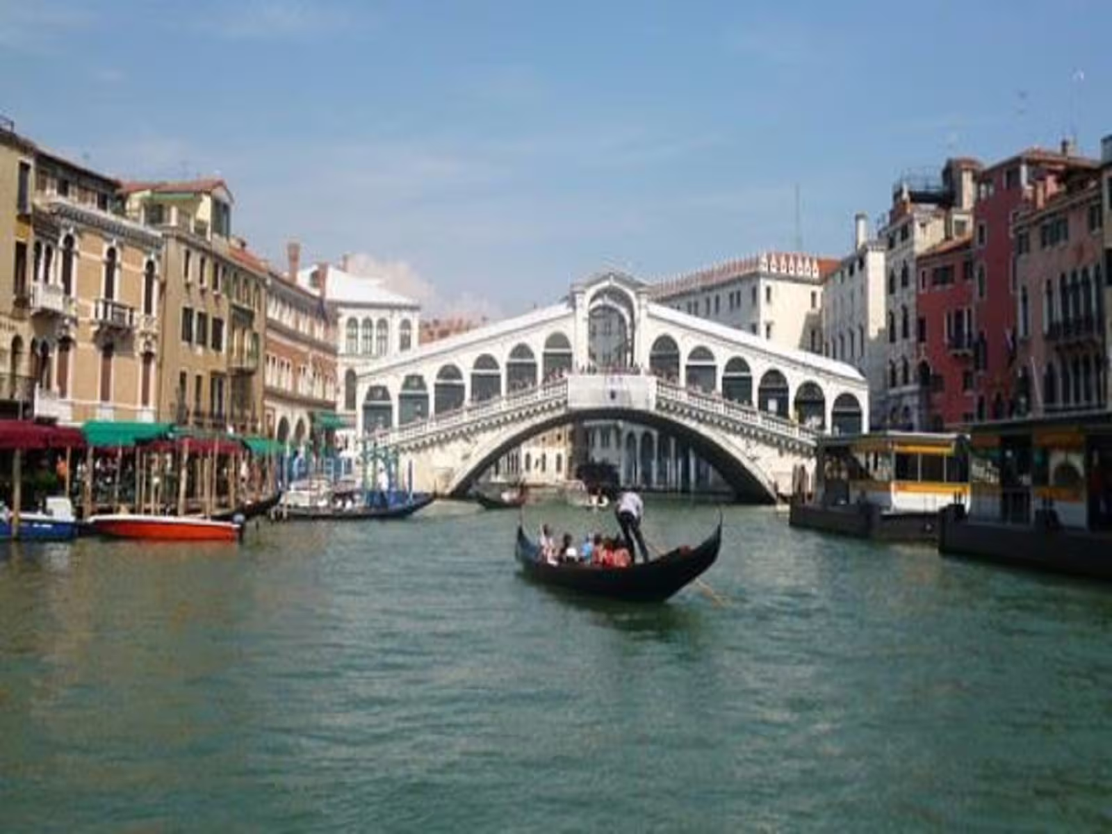 Traditional gondola with tourists gliding along Venice’s Grand Canal toward the iconic Rialto Bridge on a guided tour