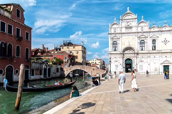 Gondolier steering past historic palaces and a stone bridge near Scuola Grande di San Marco on a Venice private canal tour
