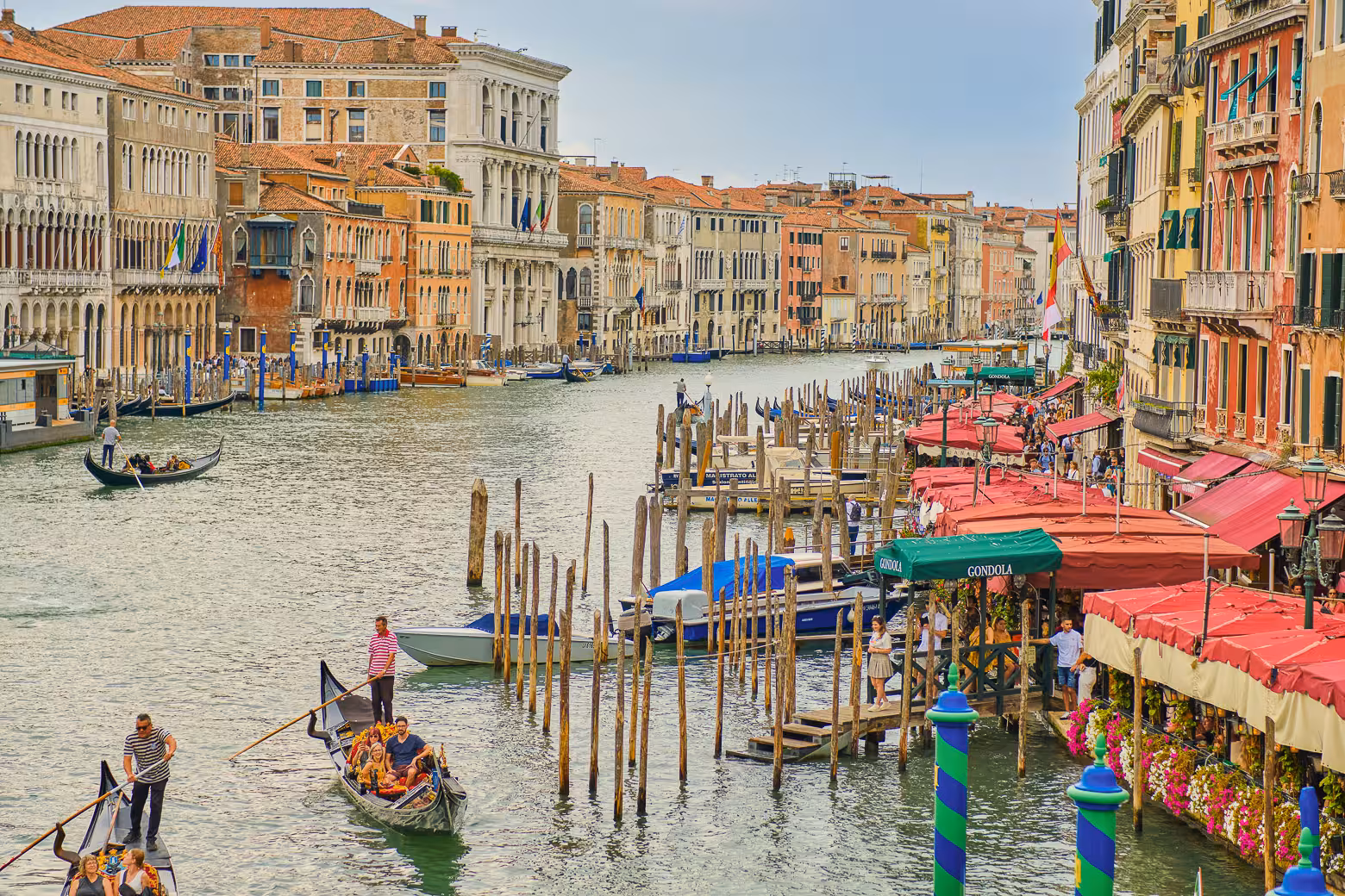 Gondolas glide along Venice's bustling Grand Canal lined with colorful buildings and lively cafes.