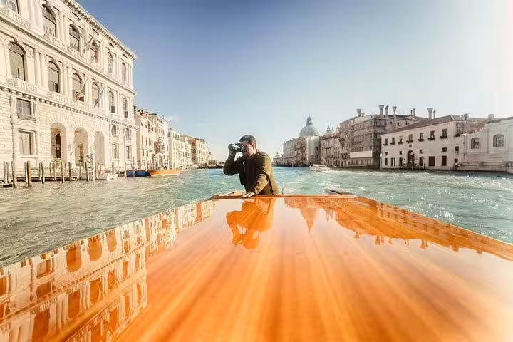 Tourist capturing Venice's stunning Grand Canal from a sleek wooden boat during a private boat tour experience.