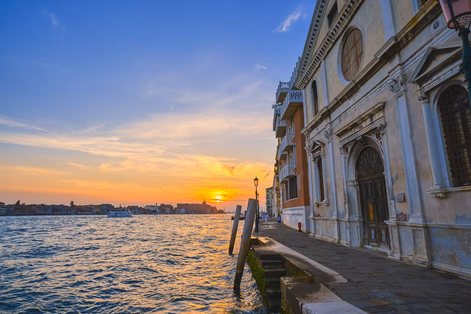 Venice waterside promenade at sunset with historic architecture and vibrant sky reflecting on the Grand Canal.