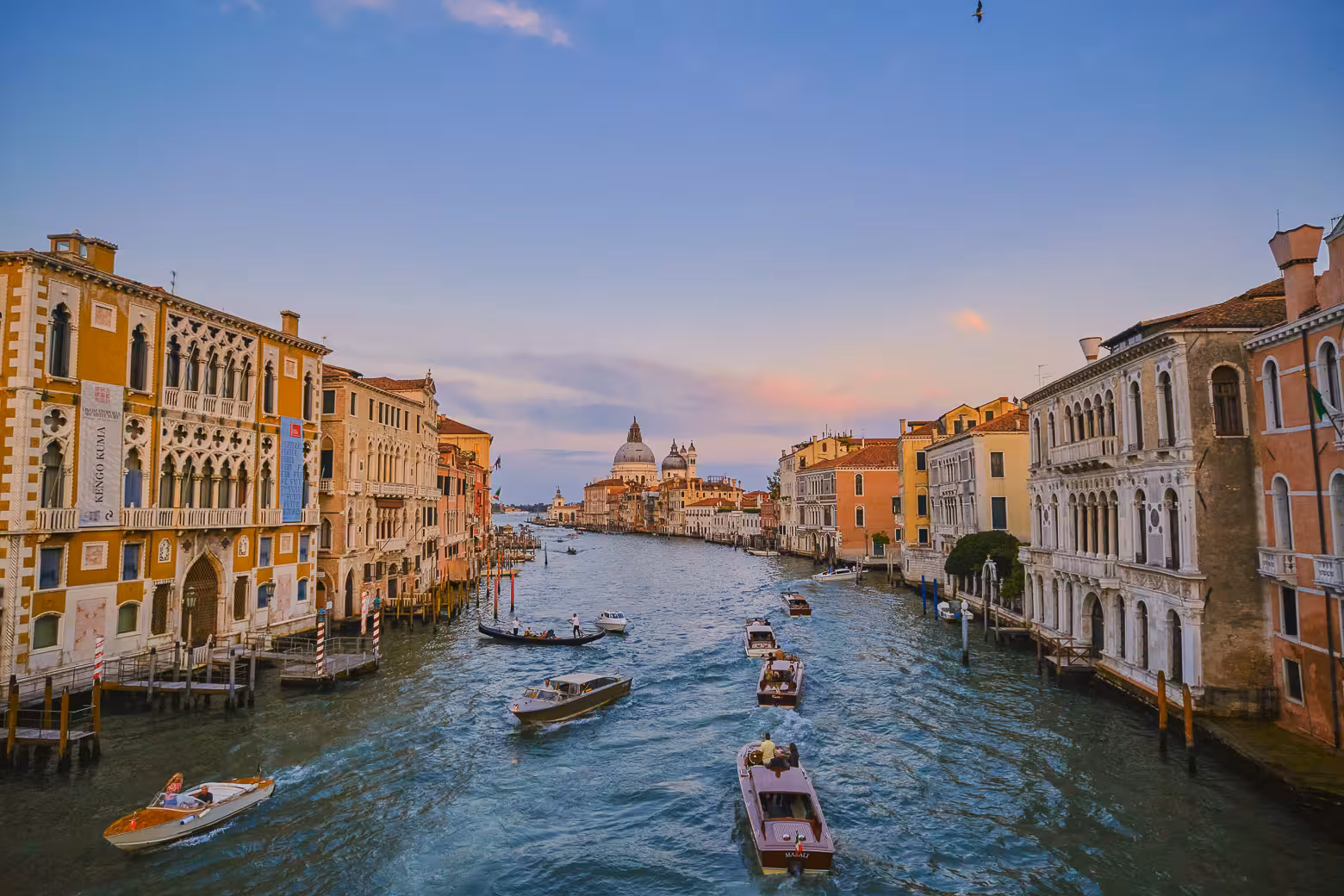 Picturesque view of Venice's Grand Canal with boats navigating between historic buildings during a vibrant sunset.