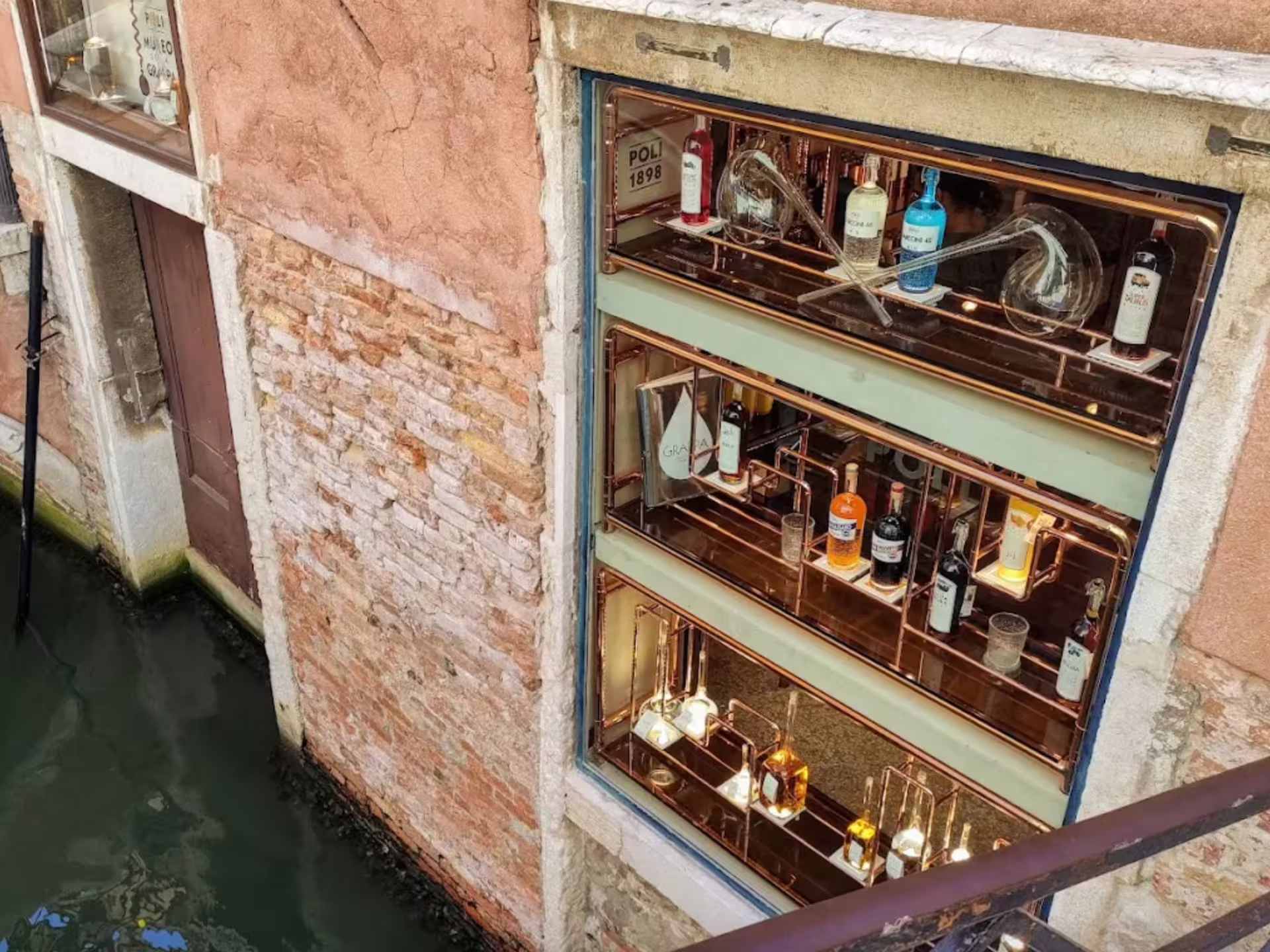Canal-side view of a Venice grappa shop with a variety of bottles displayed elegantly in the window.