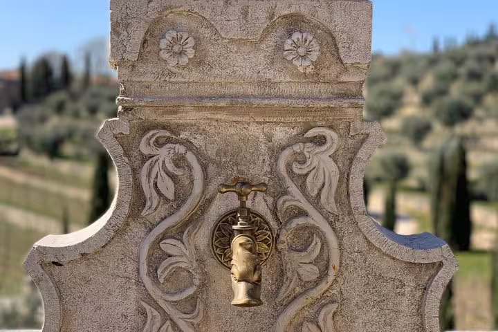 Intricately carved stone fountain with brass tap in scenic Italian countryside between Venice and Milan.