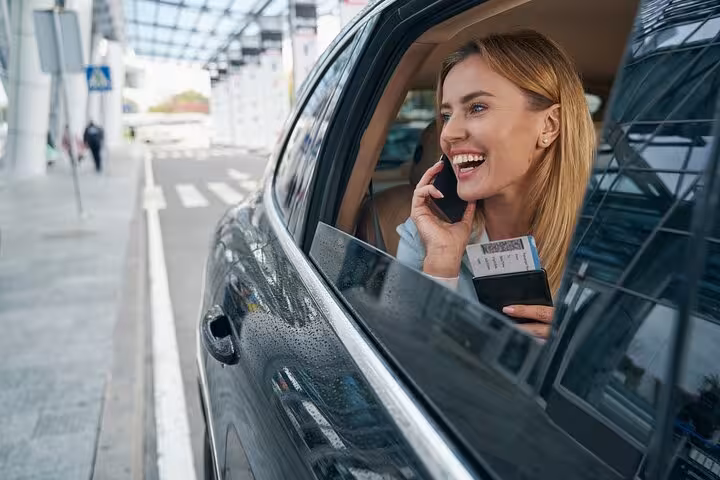 Smiling woman in a car, holding a passport and talking on the phone, enjoying her private transfer from Venice to Ravenna port.