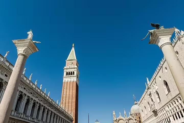 Explore Venice's iconic St. Mark's Square with its historic columns and Campanile against a clear blue sky.