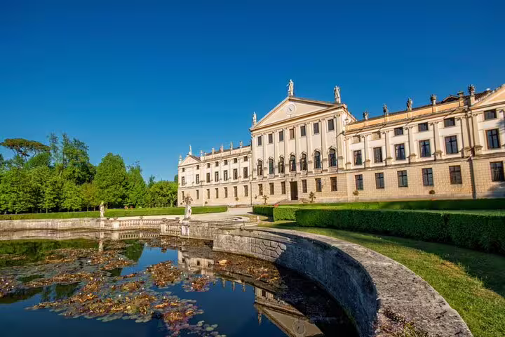 Elegant Venetian villa with ornate facade, statues, and lily pond surrounded by lush gardens