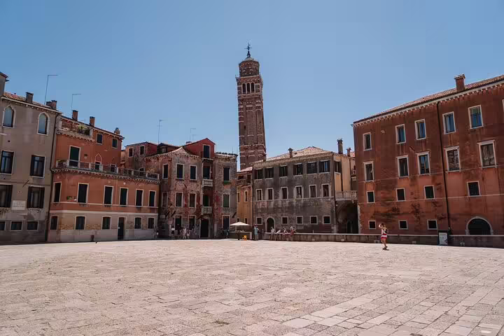 Sunlit Venice campo square with terracotta buildings and leaning bell tower in background