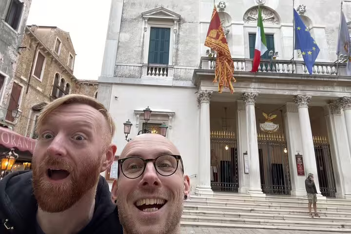 Two smiling tourists taking a selfie in front of Teatro La Fenice opera house in Venice, Italy