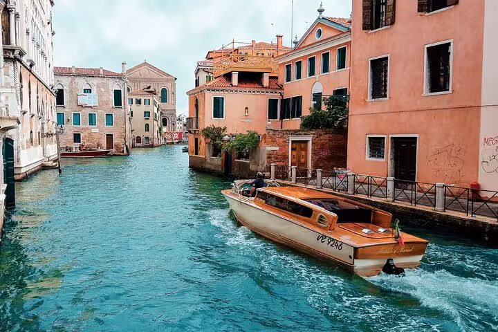 Scenic view of a private water taxi cruising through a picturesque Venetian canal near historic buildings.
