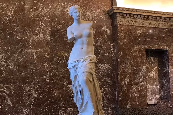 Venus de Milo marble statue displayed against brown marble wall in the Louvre Museum