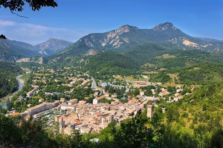 Aerial view of a historic French village nestled in a green valley with mountains and a river in the background