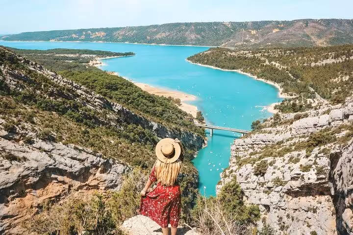 Woman in red dress overlooking turquoise Lake Sainte-Croix and Verdon Gorge from rocky viewpoint