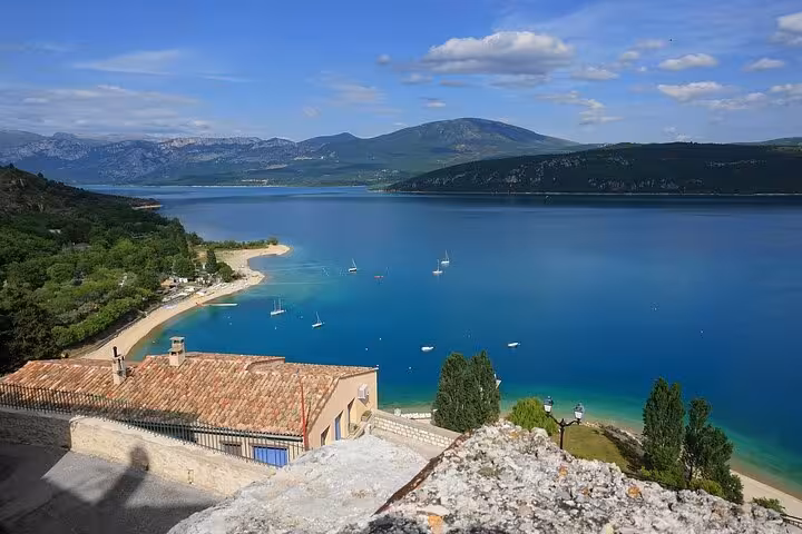 Panoramic view of turquoise Lake Sainte-Croix with sailboats, sandy beach, and mountain backdrop at Verdon Gorge