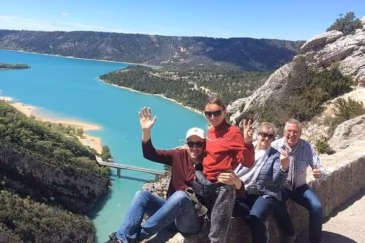 Happy tourists enjoying the scenic overlook at Verdon Gorge with a view of the turquoise lake and lush landscapes.