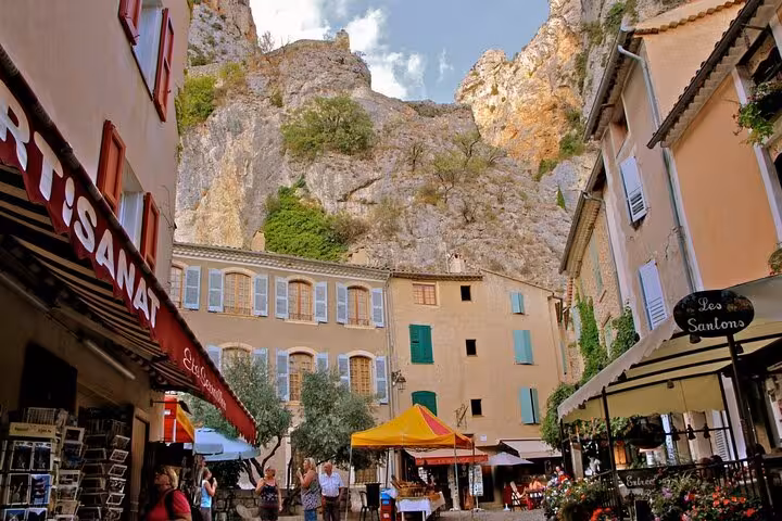 Charming village square in Moustiers-Sainte-Marie with limestone cliffs, colorful shutters, and market stalls