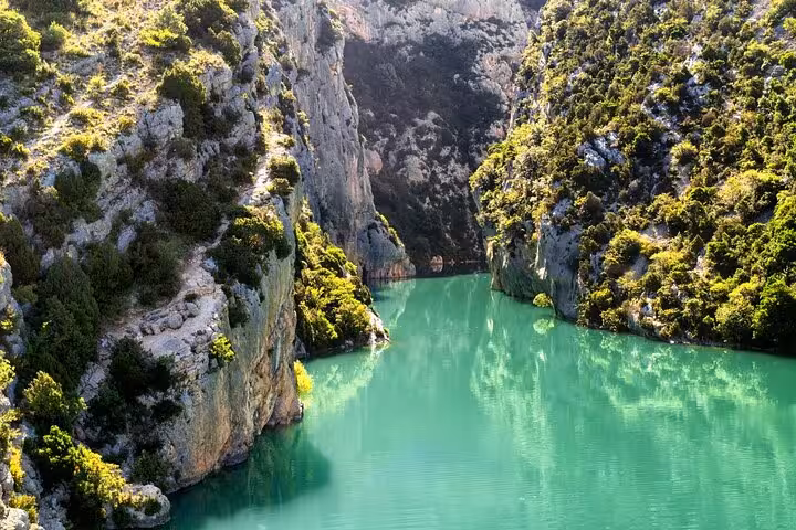 Turquoise green waters of Verdon Gorge canyon surrounded by limestone cliffs and lush vegetation