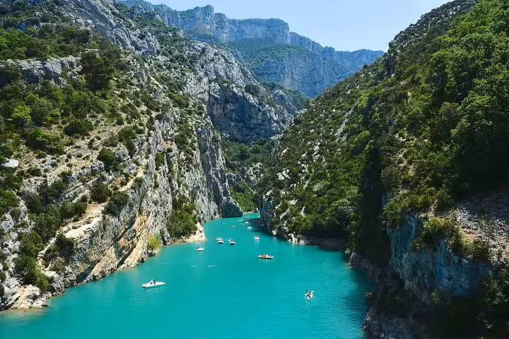Turquoise waters of Verdon Gorge canyon with small boats surrounded by lush green cliffs