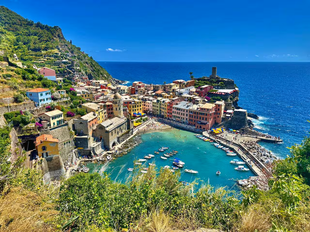 Stunning view of Vernazza's colorful seaside village and harbor under a clear blue sky in Cinque Terre, Italy.