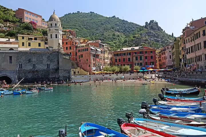 Boats moored in Vernazza harbor with pastel houses and beach, included on La Spezia to Cinque Terre return ship transfer