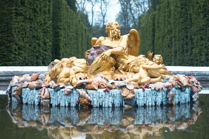 Golden baroque fountain sculpture with cherubs and seashells at the Palace of Versailles gardens
