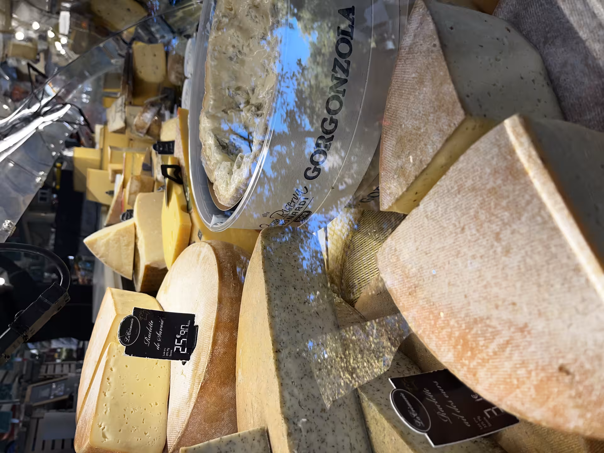 Artisan cheese display at Versailles market featuring Gorgonzola, Raclette de Savoie and aged French cheeses