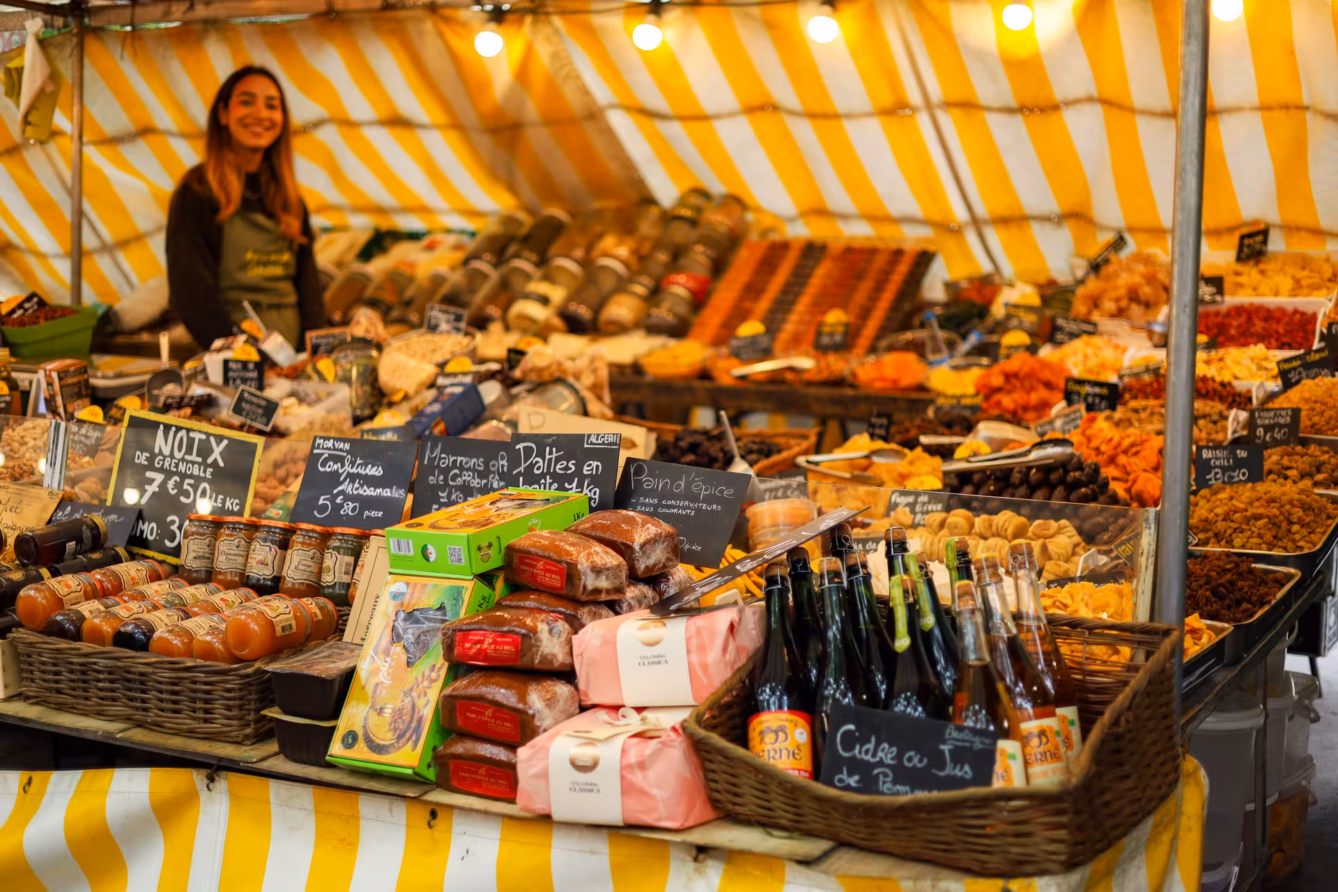 French market stall with nuts, dried fruits, pain d'épice and cider bottles at Versailles food market