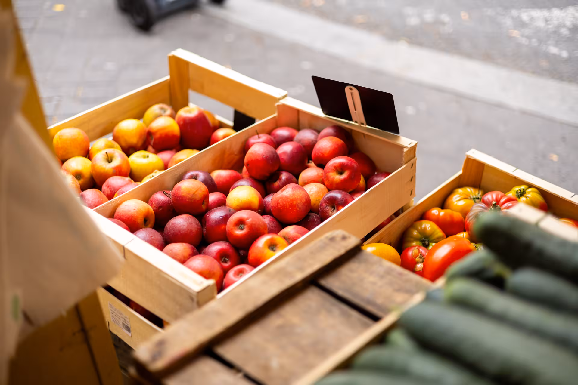 Wooden crates of fresh red apples and heirloom tomatoes at a Versailles outdoor market stall