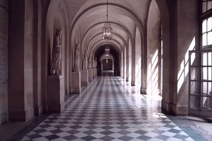 Grand arched corridor with checkered marble floors and classical statues at Palace of Versailles, Paris