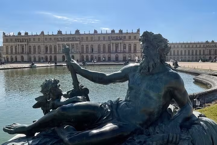 Bronze fountain statue at Palace of Versailles gardens with grand château facade in background