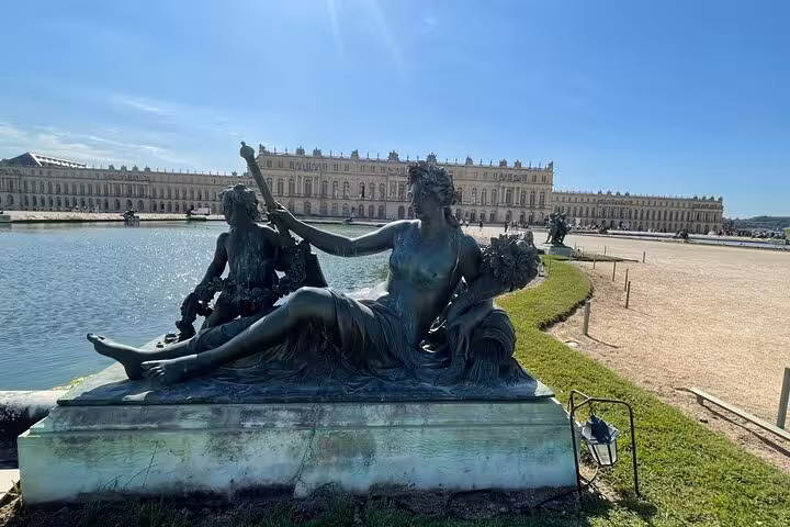 Bronze sculpture at the reflecting pool with the Palace of Versailles facade in the background