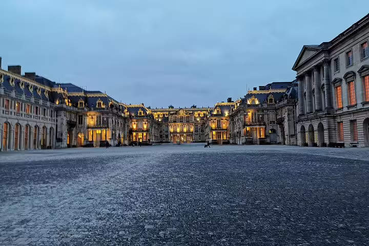 Versailles Palace courtyard at dusk on guided tour with skip-the-line tickets, illuminated royal facade