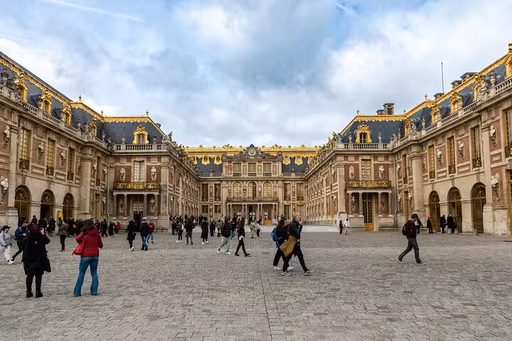 Visitors in the Versailles palace courtyard beneath gold-trimmed roofs on a guided garden and palace tour