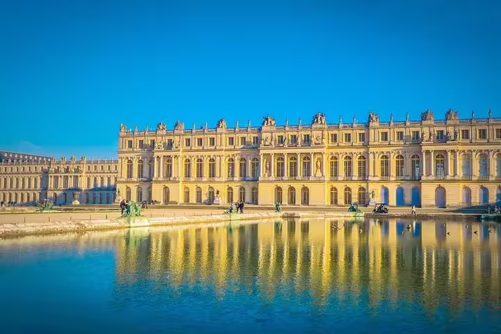 Versailles Palace façade reflected in the water under blue sky, seen on a private guided day trip from Paris