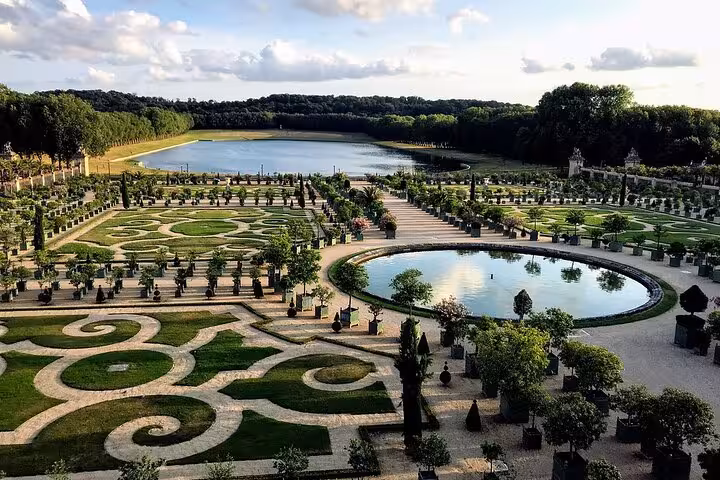 Aerial view of Versailles Palace ornate formal gardens with geometric patterns, fountains, and tree-lined pathways