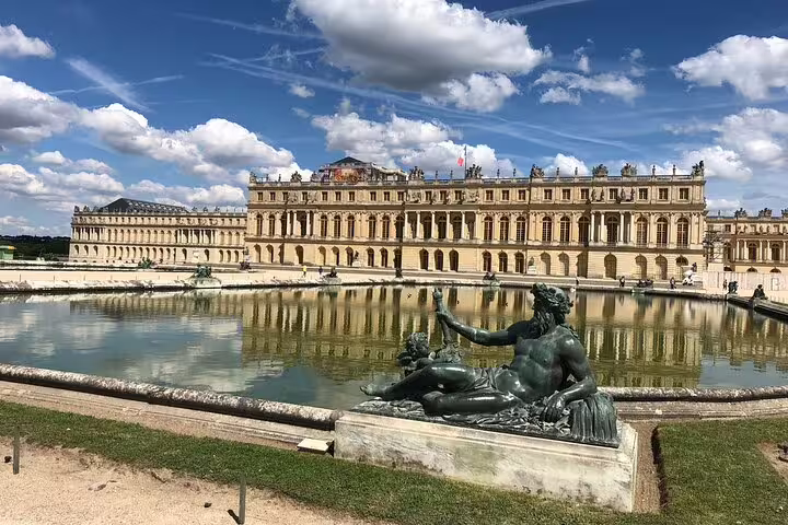 Palace of Versailles façade reflected in garden fountain with bronze reclining statue in foreground