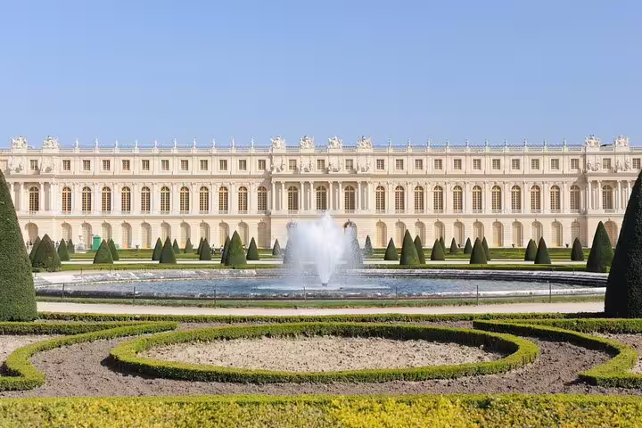 Palace of Versailles garden with ornamental hedges, topiary trees, and fountain on sunny day