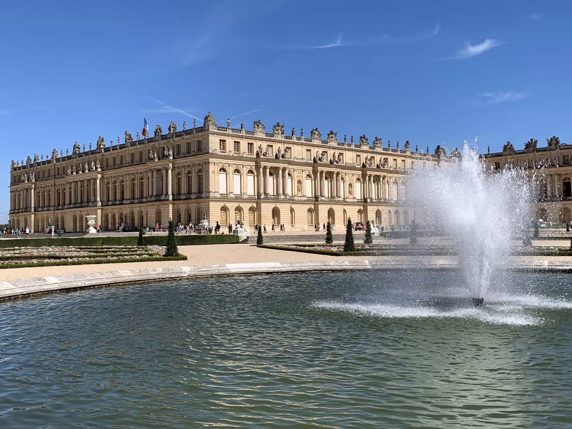 Palace of Versailles garden facade with ornate sculptures, manicured hedges, and a fountain in the foreground
