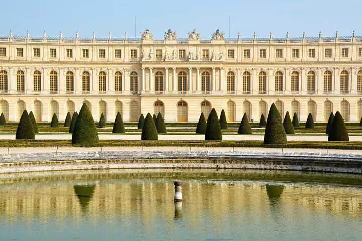 Palace of Versailles garden facade with trimmed conical topiaries reflected in a fountain pool