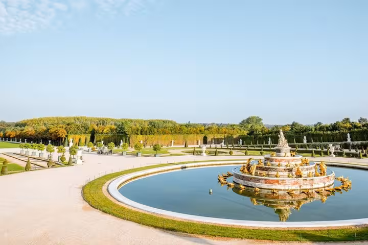 Ornate golden Latona Fountain in the formal gardens of the Palace of Versailles on a sunny day