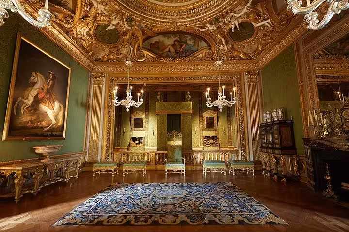 Ornate gilded hall at Palace of Versailles with green walls, chandeliers, baroque ceiling, and equestrian portrait