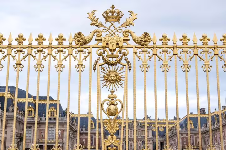 Golden ornate gates of the Palace of Versailles with sun king emblem and royal crown detail
