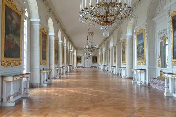 Grand gallery hall at Palace of Versailles with crystal chandeliers, gold-framed paintings, and ornate white columns